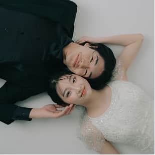 黒のタキシードを着た男性と白のドレスを着た女性が、白い背景の上で笑顔で寄り添っている。