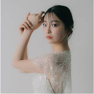 白い背景の前で、ビーズ刺繍が施されたドレスを着た女性が横顔を向けている。