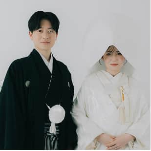 黒い着物を着た男性と、白い和装をした女性が並んで微笑んでいる写真。