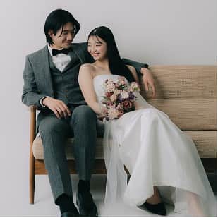 ソファに座る新郎新婦が互いに微笑み合い、花束を持った新婦は白いドレスを着ている。